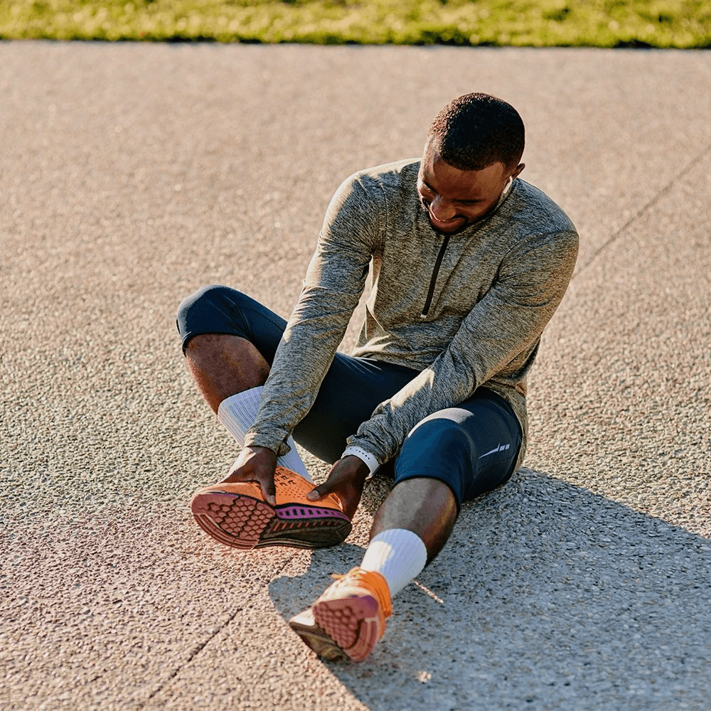 Runner sits on ground and holds his foot in pain