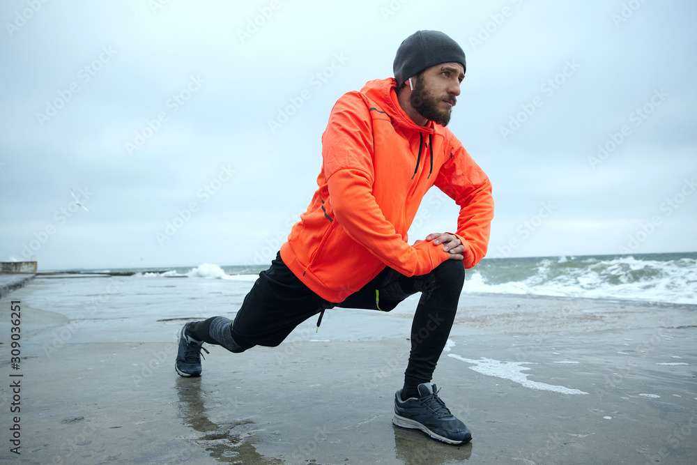 young man with orange jacket stretching on beach